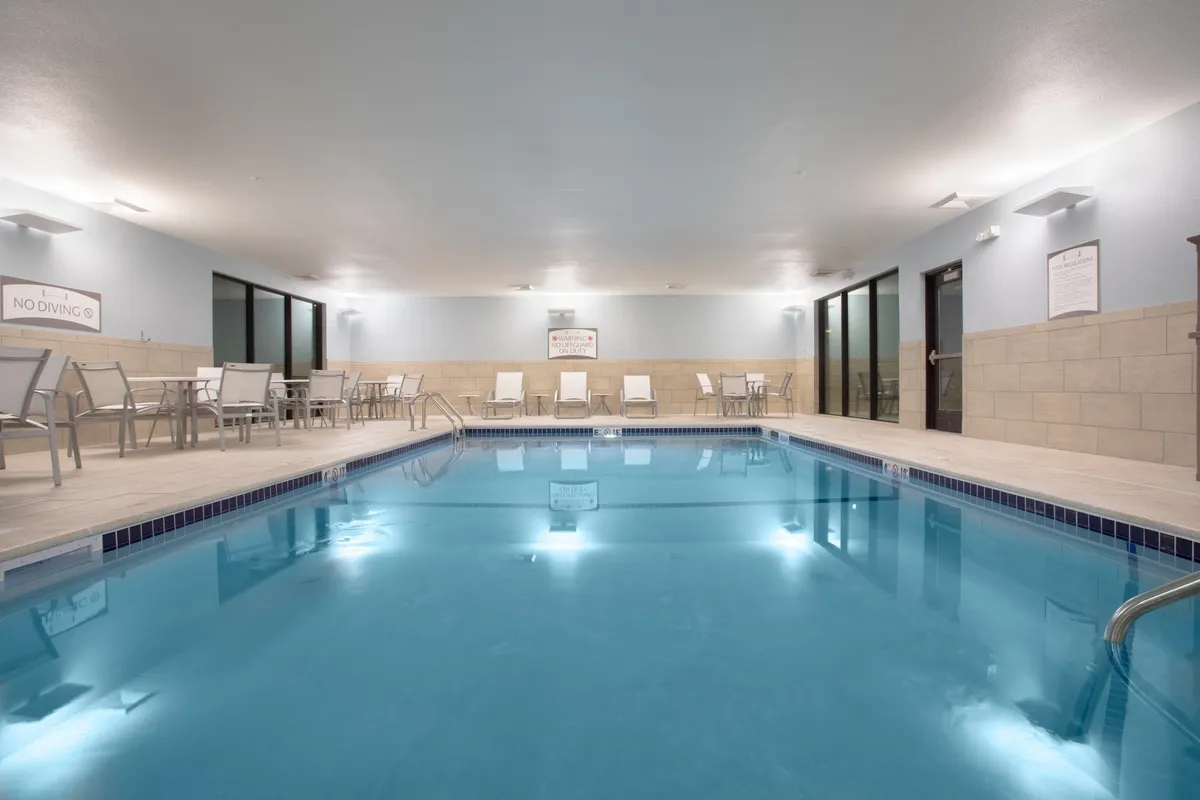 A tranquil indoor swimming pool with inviting lounge chairs set along the tiled poolside, accented by soft poolside lighting. The serene atmosphere is perfect for relaxation or a refreshing swim, and the clean, modern design speaks to both comfort and luxury.