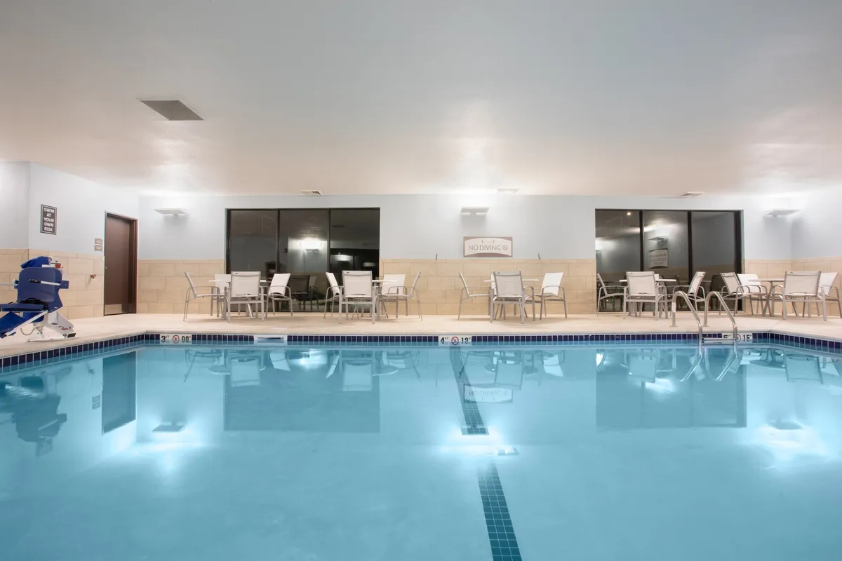 This image features a spacious swimming pool area with comfortable seating arrangements and large windows offering views of the outdoors. The atmosphere is lively yet relaxed, with guests enjoying a swim or unwinding by the water, evoking a sense of community and recreation.