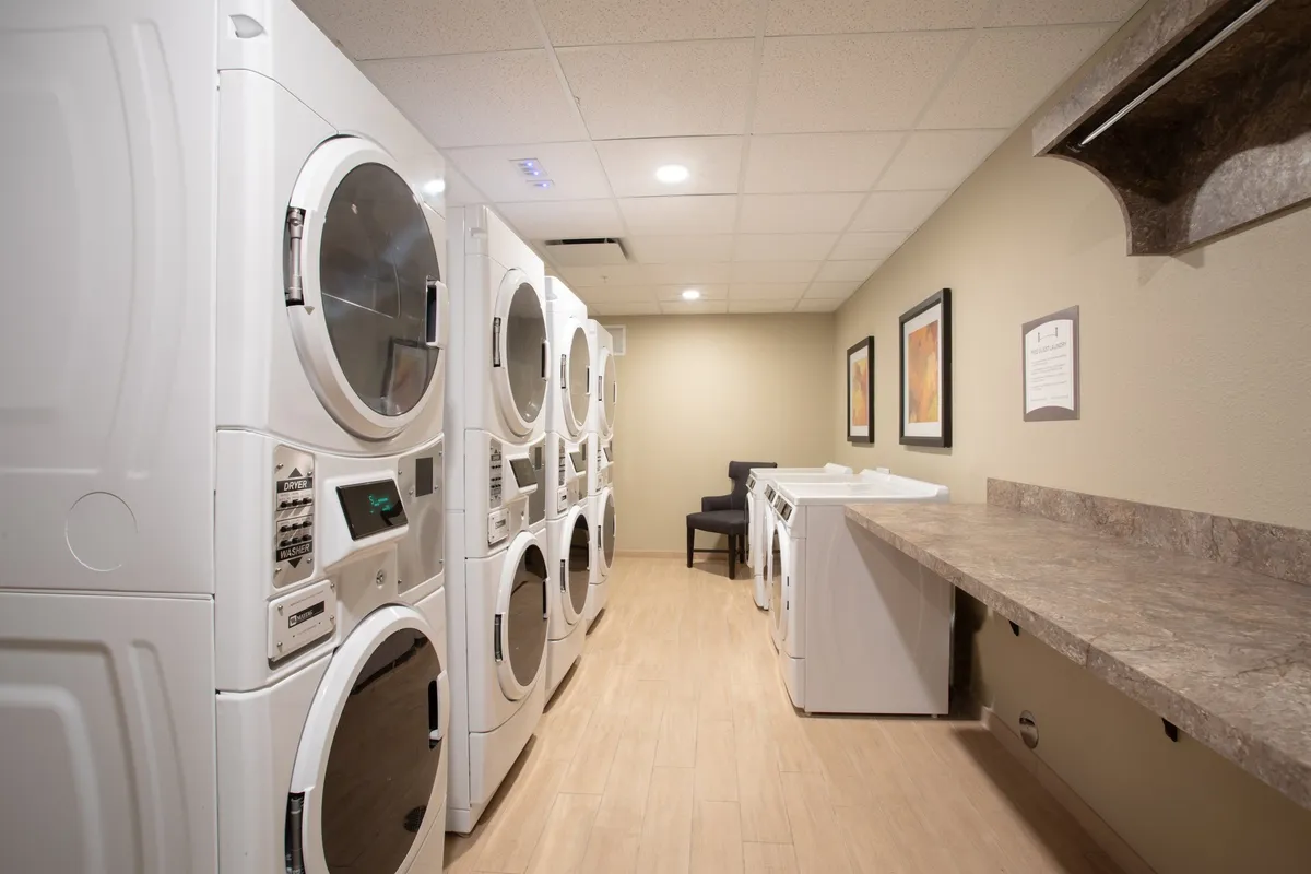 A practical laundry facility with multiple washing machines and dryers, a countertop for folding clothes, and a seating area for waiting. The space is clean and efficiently organized, making it convenient for extended stays.