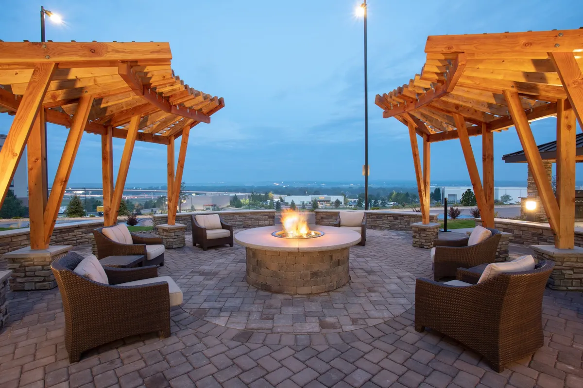 An inviting exterior communal fire pit area featuring a wooden structure, comfortable seating, and a cozy atmosphere set up for gathering, storytelling, and relaxing after outdoor adventures. The space is surrounded by landscaping that hints at a connection to nature and the outdoors.
