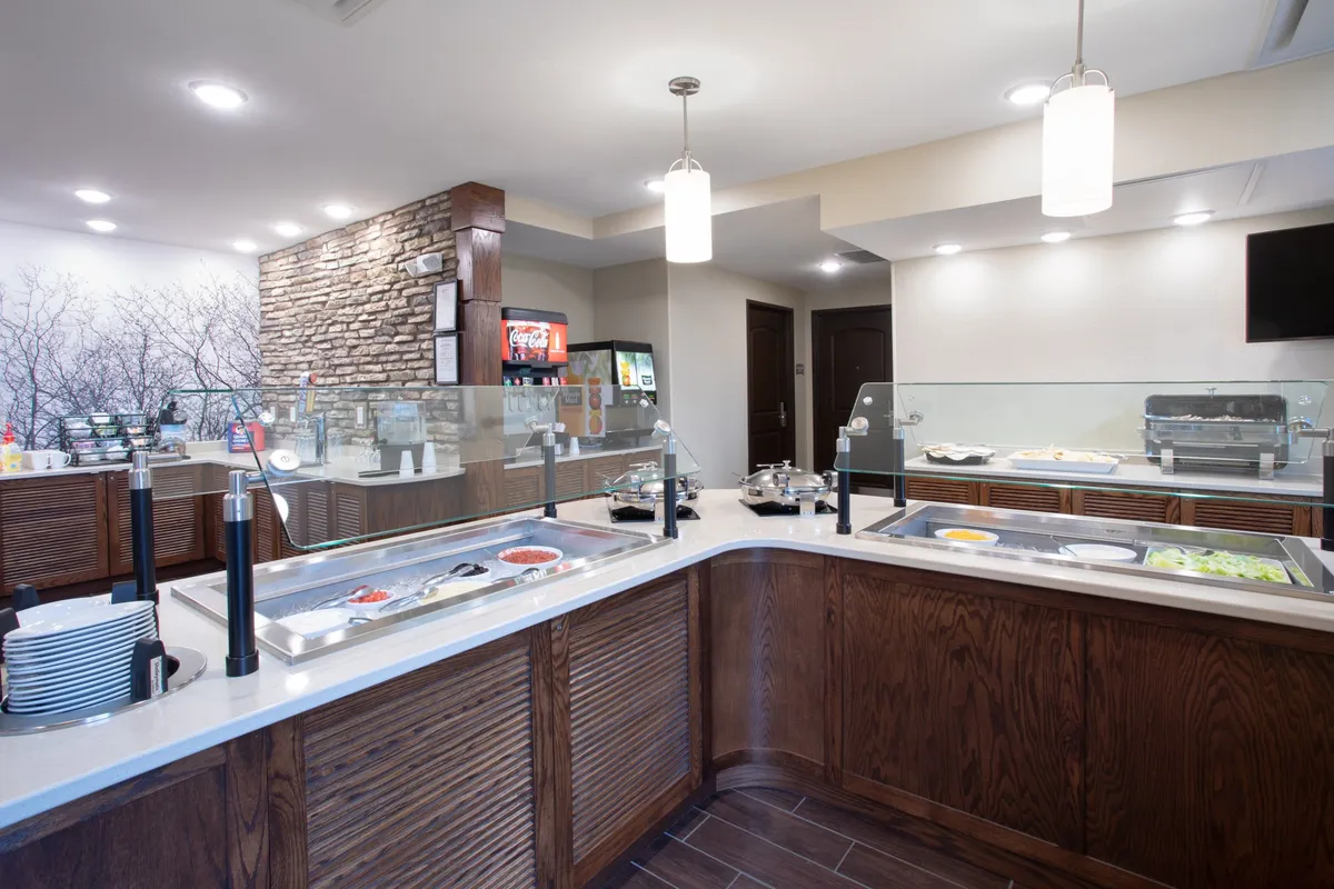 An inviting buffet area with attractive food displays and a beverage station, set against a decorative stone wall. The space is bustling with opportunities for self-serve dining and casual breakfast meetings, creating a welcoming atmosphere for guests to start their day.