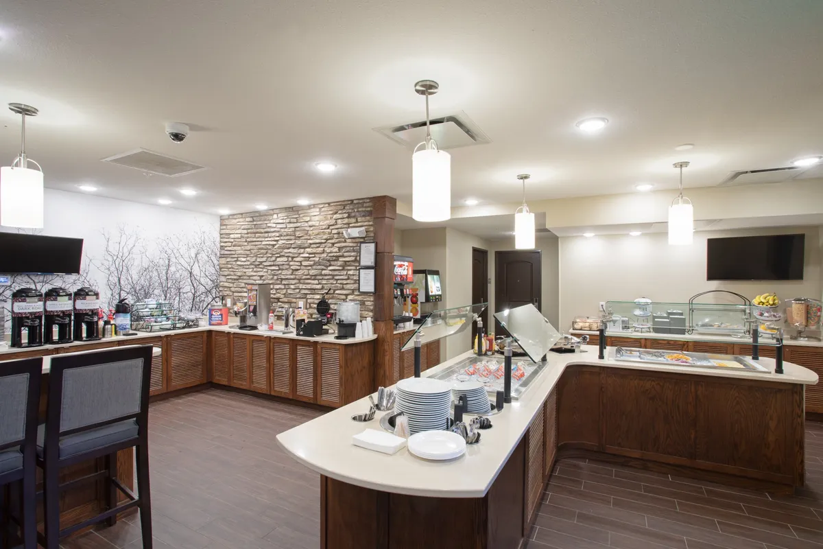 A relaxed interior breakfast buffet area featuring a coffee station, stone feature wall, and inviting seating. Guests are seen enjoying breakfast, socializing, or working on laptops, which underscores the communal and welcoming nature of the space.